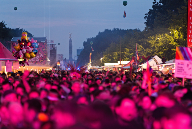 Eine gro%C3%9Fe Menge auf einem nächtlichen Musikfestival mit bunten Lichtern, Ballons, Zelten, Bannern, Fahnen, Bäumen, einem Turm und einem sternenklaren Himmel im Hintergrund.