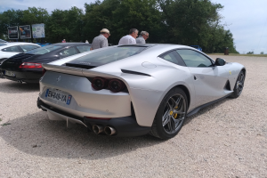 Roter Ferrari 812 Superfast beim Goodwood Festival of Speed, umgeben von Menschen mit Mützen, Bäumen, Texttafeln und einem bewölkten Himmel im Hintergrund.