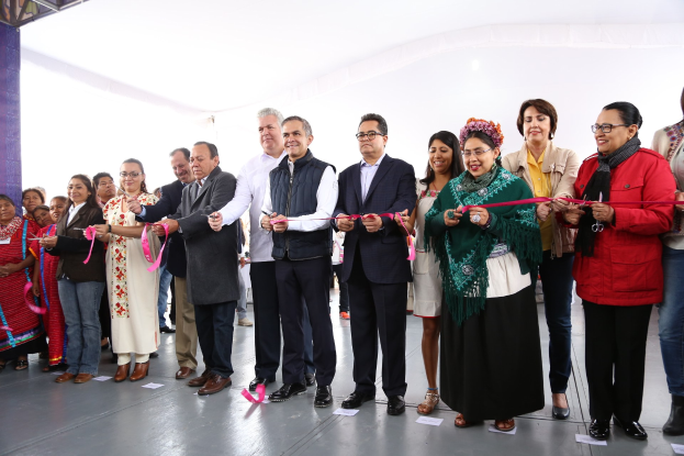 Eine Gruppe von Menschen, die mit Schere lächeln und eine Schnur vor einer Menge schneiden, mit einer Säule links, Papieren auf dem Boden und einem weißen Tuch im Hintergrund.