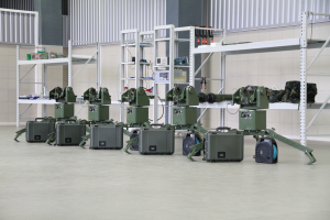 Eine Gruppe von Militärrobotern auf einem Boden umgeben von Koffern und anderen Gegenständen, mit einer Wand und einem Geländer im Hintergrund.