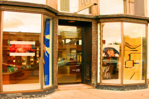 Ein Gebäudeinneres mit einem Tisch, Wandplakaten und Kosmetikartikeln auf der linken Seite.