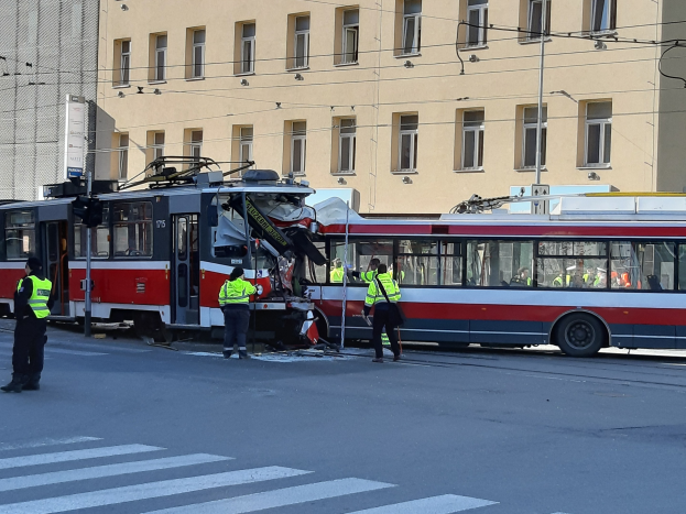 Eine rote und weiße Tram, die auf der Straße in einen Unfall verwickelt ist, mit ein paar Menschen in der Nähe und einem Gebäude im Hintergrund.