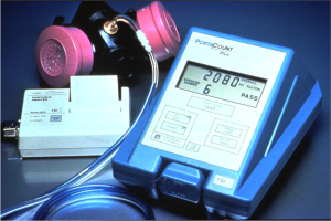 Eine Gasmaske auf einem Tisch neben einem elektronischen Gasdetektorgerät mit einem angeschlossenen Kabel.