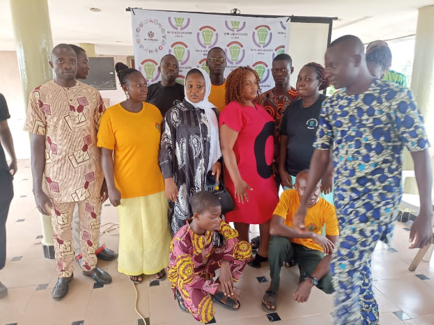 Eine Gruppe von Menschen vor einer Banner mit der Aufschrift "Advocates in Ghana: Ein Schritt-für-Schritt-Führer", umgeben von Stühlen, Säulen, einem Fernseher und einer Decke mit Deckenleuchten.