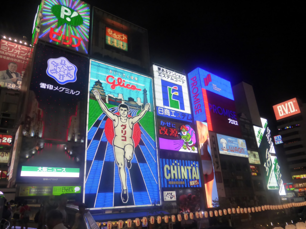 Eine belebte Stadtstraße bei Nacht, erhellt von hellen Lichtern aus Gebäuden und Werbetafeln, mit Menschen, die die Straße entlanggehen und dekorativen Lichtern am Boden.