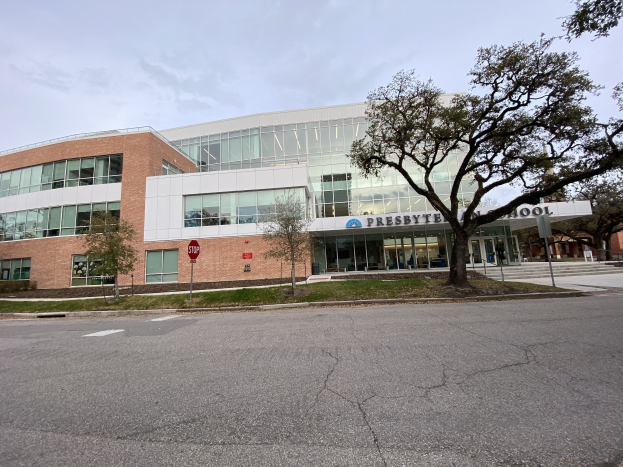 Presbyte Middle School, ein großes Gebäude mit vielen Fenstern, umgeben von Bäumen, Gras, Schildern, Pfosten und einer Straße, mit bewölktem Himmel im Hintergrund.
