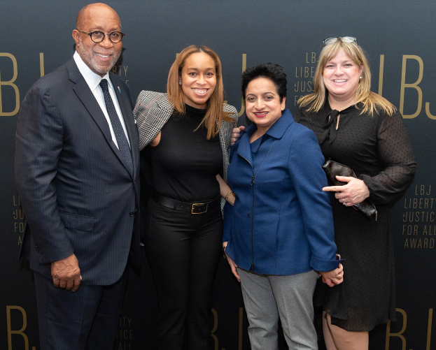Eine Gruppe von vier Menschen, die auf einem roten Teppich stehen und für ein Foto posieren, mit einem "Liberty Justice for All Awards"-Schild im Hintergrund.