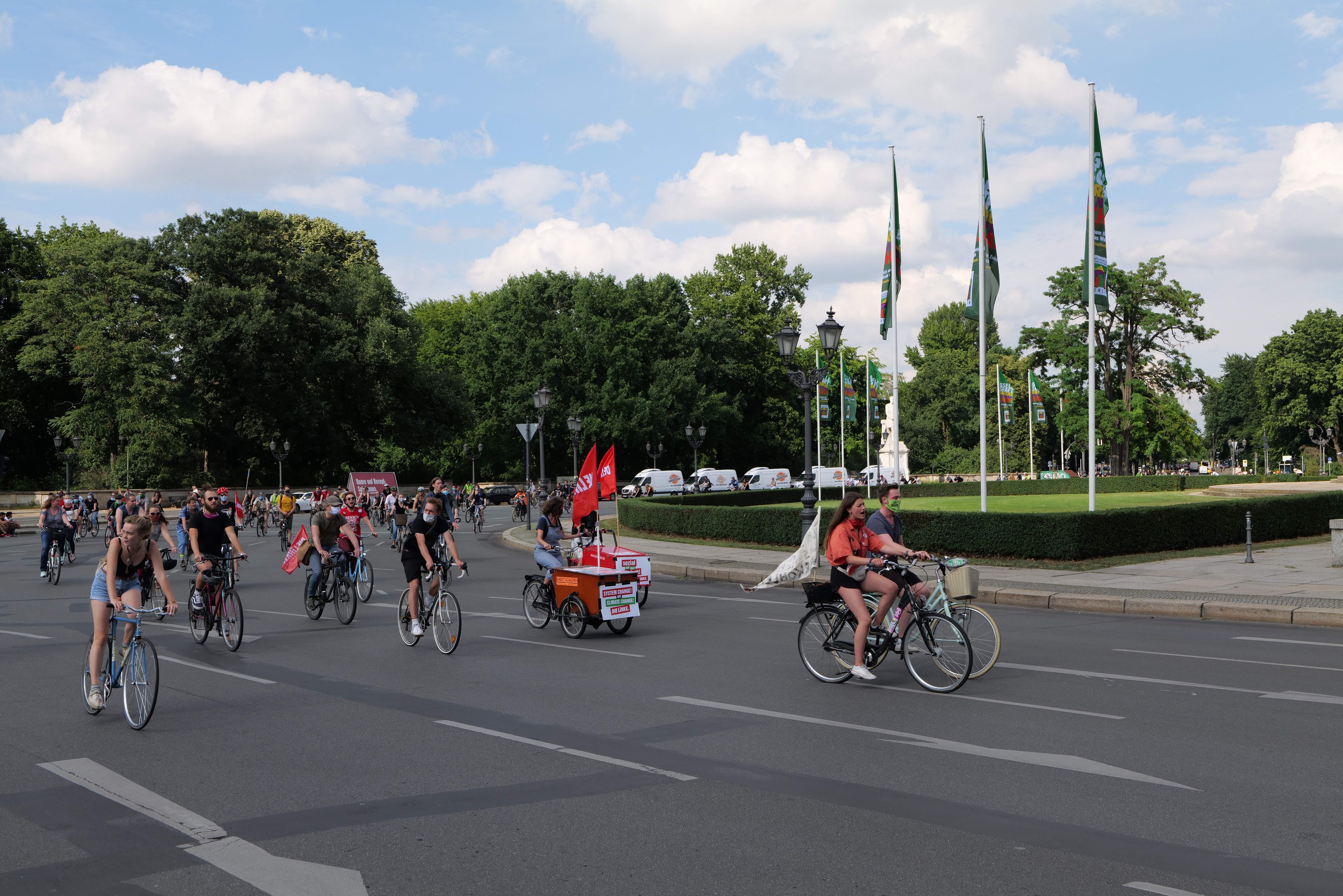 Eine Gruppe von Menschen, die auf Fahrrädern eine von Bäumen gesäumte Straße mit Laternenmasten und Fahnenmasten entlangfahren, während sie an der Paris Bike Ride 2016 teilnehmen.