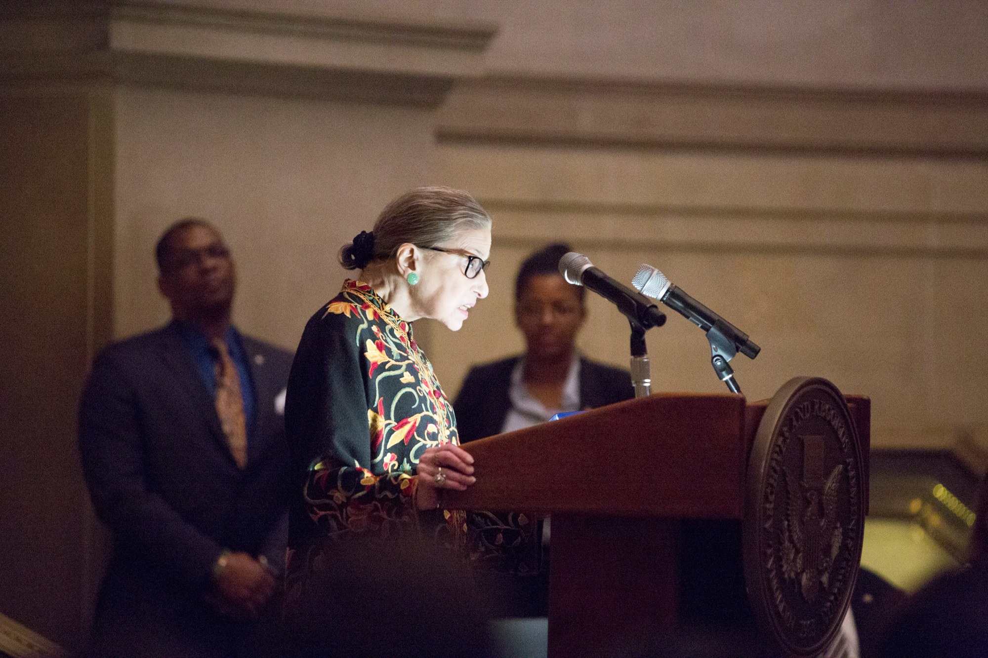 Frau in einem Anzug, die vor einem Publikum an einem Rednerpult spricht.