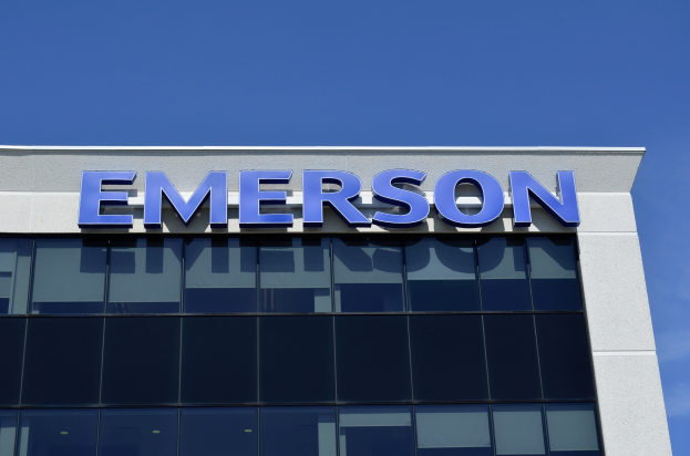 Emerson-Logo an der Außenseite eines Gebäudes mit dem Text "Emerson investiert 1,5 Milliarden USD in den USA" vor einem klaren blauen Himmel.