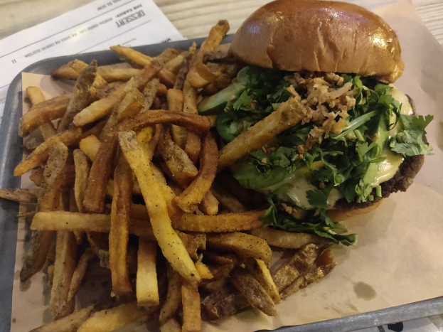 Ein Tablett mit einem mit Salat, Tomate und Zwiebeln belegten Hamburger, goldenen knusprigen Pommes frites und einem Blatt Papier auf einem Tisch.