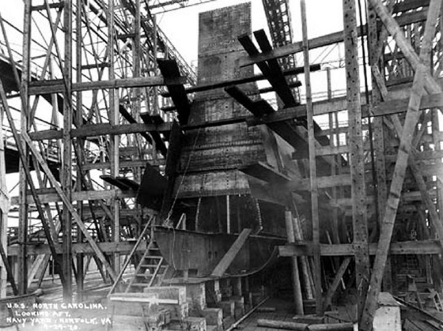 Schwarzes und weißes Foto eines Schiffes in einem Schiffbauwerk, mit hölzernen Pfählen und Treppen im Vordergrund und Himmel im Hintergrund, mit dem Text "Marinebewaffnung" in der linken unteren Ecke.