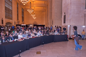 Ein Konzertbild mit einer Menge Menschen, einem Mann, der rechts Gitarre spielt und singt, einer Wand und Fenstern im Hintergrund, Lichtern oben und einem Boden unten.