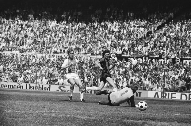 Schwarzes und weißes Foto von Männern, die auf einem Feld Fußball spielen, mit Zuschauern im Hintergrund und einer "Bundesliga 1978-79 Ajax 1-1 Hannover 96" -Fahne.