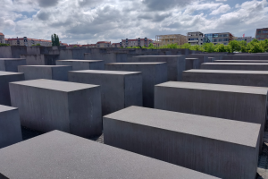 Das Holocaust-Mahnmal für die ermordeten Juden Europas in Berlin, Deutschland, zeigt zahlreiche Betonblöcke in einem Gittermuster, mit Bäumen, Gebäuden und einem bewölkten Himmel im Hintergrund.