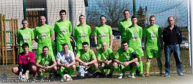 Gruppe von Männern in grünen T-Shirts, die auf einem Fußballfeld neben einem Torpfosten mit einem Ball auf dem Boden stehen.