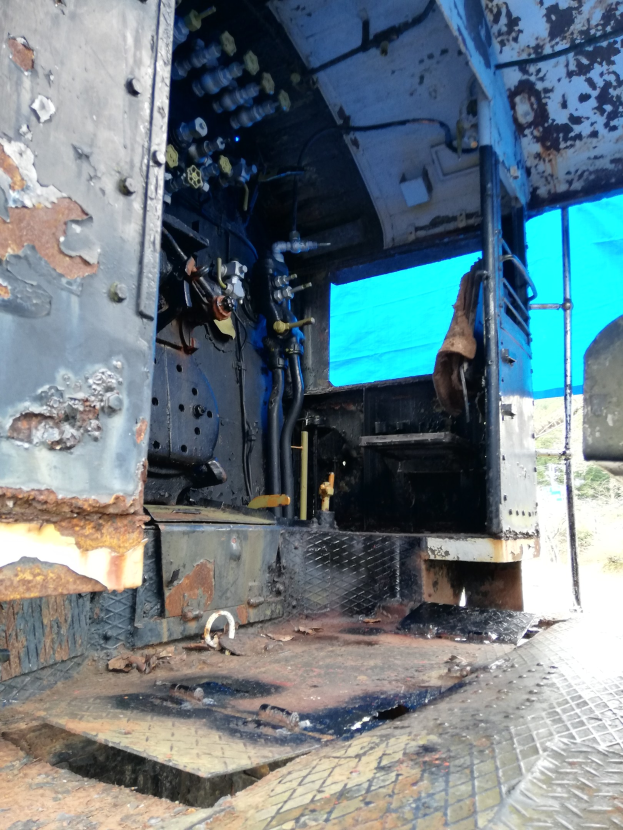 Ein verrostetes, heruntergekommenes Truck-Interieur mit sichtbaren Gebrauchsspuren, vor einem Wald und einem klaren blauen Himmel.