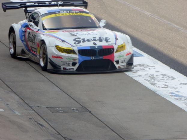 Ein strahlend blaues und weißes BMW Z4 GT3 Rennauto mit großen glänzenden Rädern, das auf einer Rennstrecke fährt und ein schlankes aerodynamisches Design sowie ein deutliches BMW-Logo aufweist.