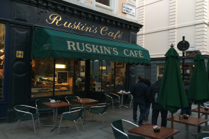 Eine Gruppe von Menschen steht vor einem Café mit der Aufschrift "Ruskin's Cafe".