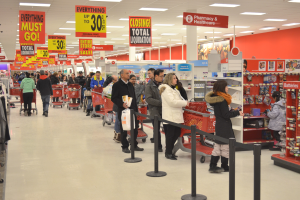 Ein volles Walmart-Geschäft mit Einkaufswagen schiebenden Kunden, umgeben von Warenpräsentationen, Schildern und Deckenlampen.