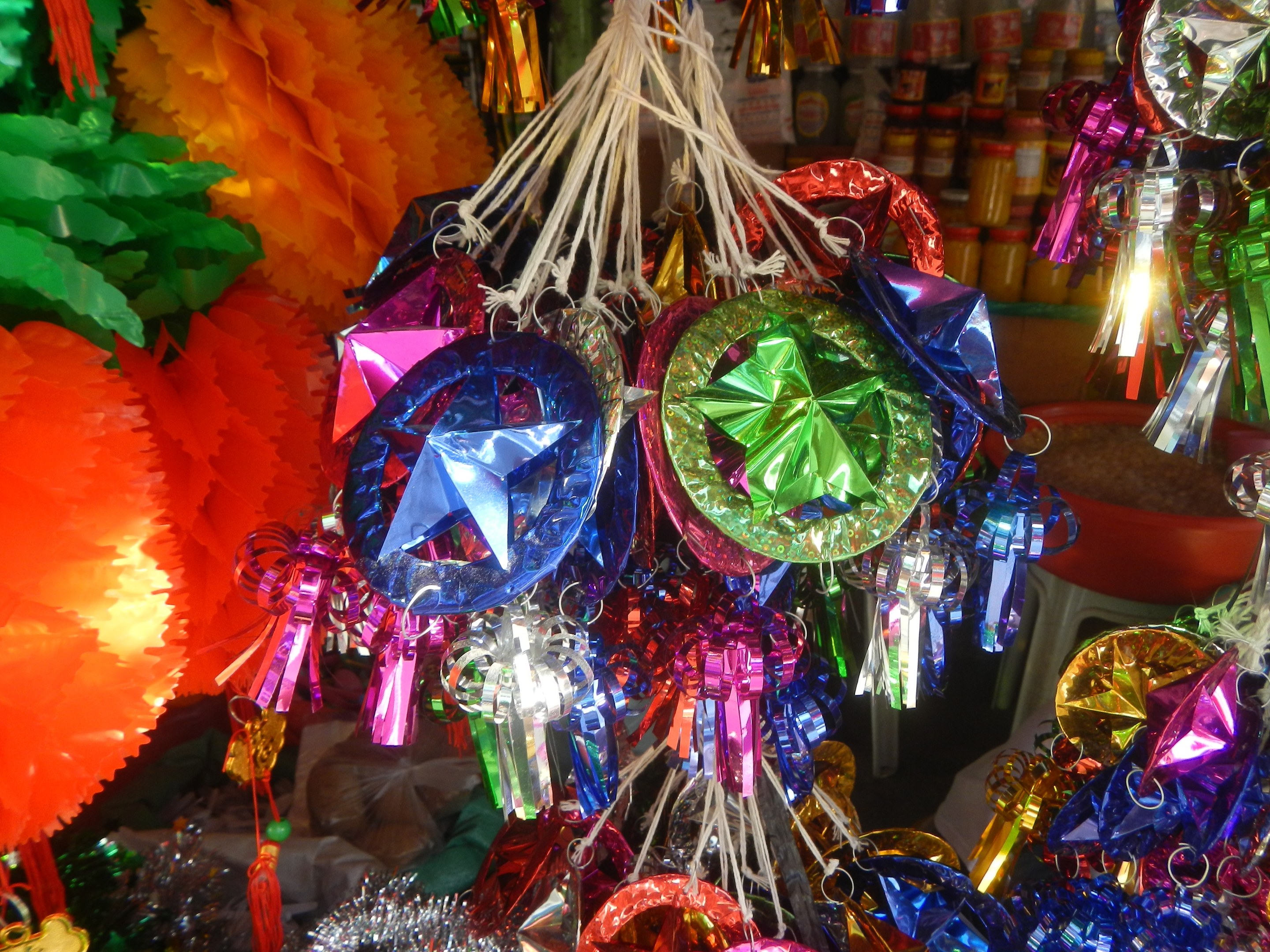 Farbenfrohe Dekorationen wie Papierlaternen und Bänder hängen von der Decke über Regalen mit Flaschen in einer festlichen Atmosphäre.
