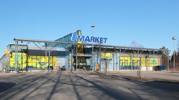 Großes Gebäude mit einer "Smart Market"-Aufschrift, umgeben von Straßenlaternen, Fahrzeugen, Bäumen und einem klaren blauen Himmel.