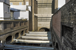 Ein Zug fährt aus einem Tunnel heraus, umgeben von Gebäuden.