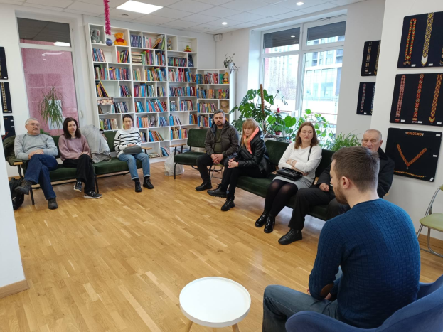 Eine Gruppe von Menschen sitzt um einen Tisch in einem Raum mit Bücherregalen, Pflanzen und Deckenleuchten und ist während einer Workshop-Diskussion über die Zukunft von Gesundheit und Wohlbefinden in Berlin, Deutschland, in ein Gespräch vertieft.