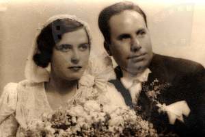 Ein Schwarz-Weiß-Foto einer Frau in einem weißen Kleid mit einem Blumenstrauß und einem Mann, der neben ihr steht und beide lächeln.