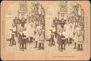 Eine Gruppe von Kindern steht vor einem Weihnachtsbaum mit einem erwachsenen Paar in der Mitte, umgeben von Rahmenfotos an der Wand.