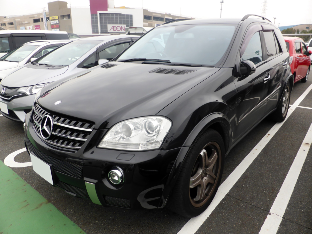 Schwarzer Mercedes-Benz ML 350 CDI BlueEfficiency auf einem Parkplatz mit Gebäuden, Pfählen, Bäumen und einem klaren blauen Himmel im Hintergrund geparkt.