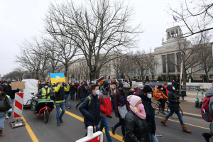 Eine große Gruppe von Menschen marschiert auf einer Demonstration die Straße in Washington, D.C. am 21. Januar 2020 entlang, mit Schildern und Transparenten, einige fahren Fahrräder, mit Bäumen, Schildern und einem Gebäude im Hintergrund unter einem klaren blauen Himmel.