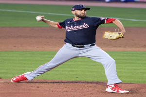 Ein Baseballspieler in einer Mütze und Handschuh wirft auf einem grünen Feld, mit Menschen und Texttafeln im Hintergrund, die einen World-Series-Sieg der Washington Nationals anzeigen.