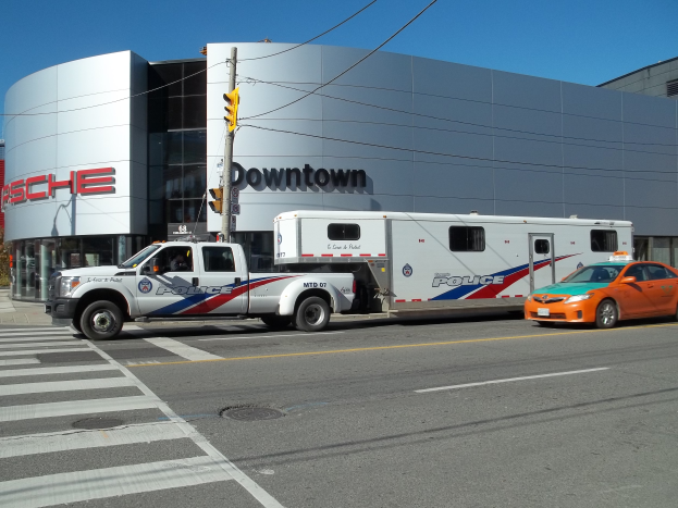 Ein Polizei-Lkw steht vor einem Gebäude mit Text darauf, mit einer Ampel mit Stange und Drähten im Vordergrund und Bäumen und einem klaren blauen Himmel im Hintergrund.