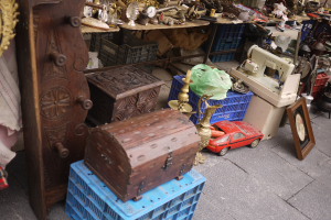 Ein Flohmarkt mit verschiedenen Gegenständen, darunter Holzkisten, ein Spielzeugauto, eine Nähmaschine, ein Foto Rahmen, eine Uhr und andere Gegenstände auf Tischen.